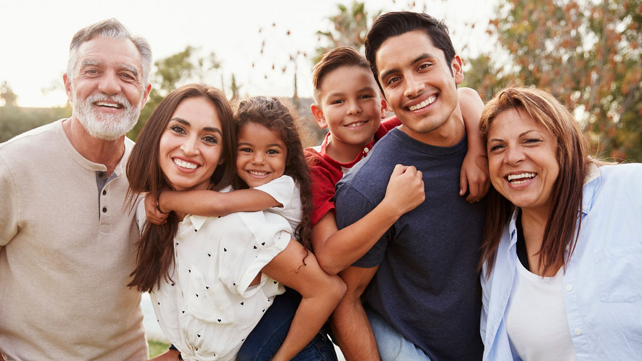 Three generation Hispanic family standing in the park, smiling to camera, selective focus