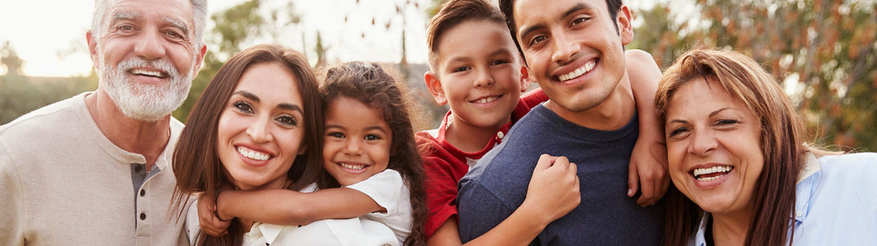 Three generation Hispanic family standing in the park, smiling to camera, selective focus