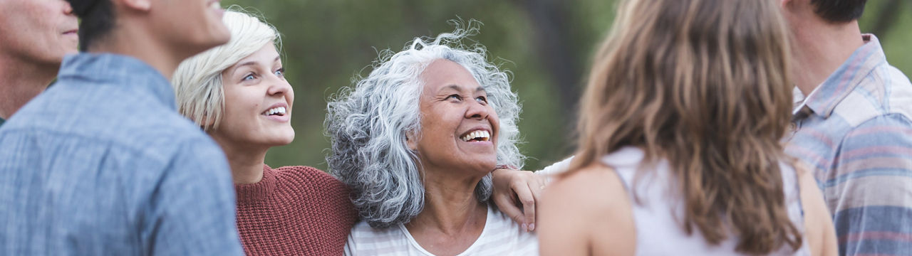 A multiethnic group of friends embrace and energetically chat with one another. They're in a loose circle.