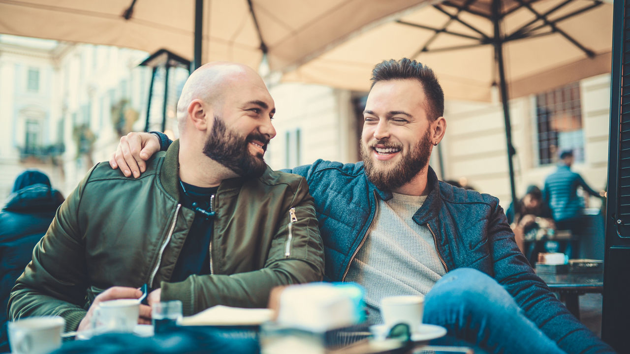 Two smiling handsome friends drinking coffee and talking at favorite coffee place