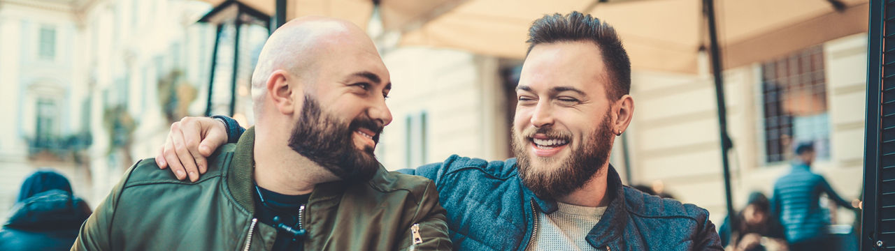 Two smiling handsome friends drinking coffee and talking at favorite coffee place