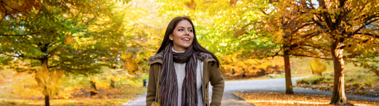 Attractive woman walks in an autumn park in the city with golden leaves and sunshine