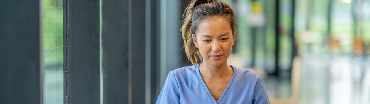 A woman wearing scrubs diligently studies at a desk in a modern educational building