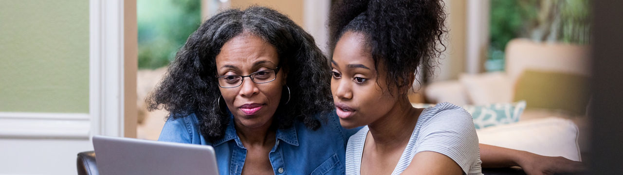 Young woman and her mature mom look at something on a laptop as the young woman studies for a college exam