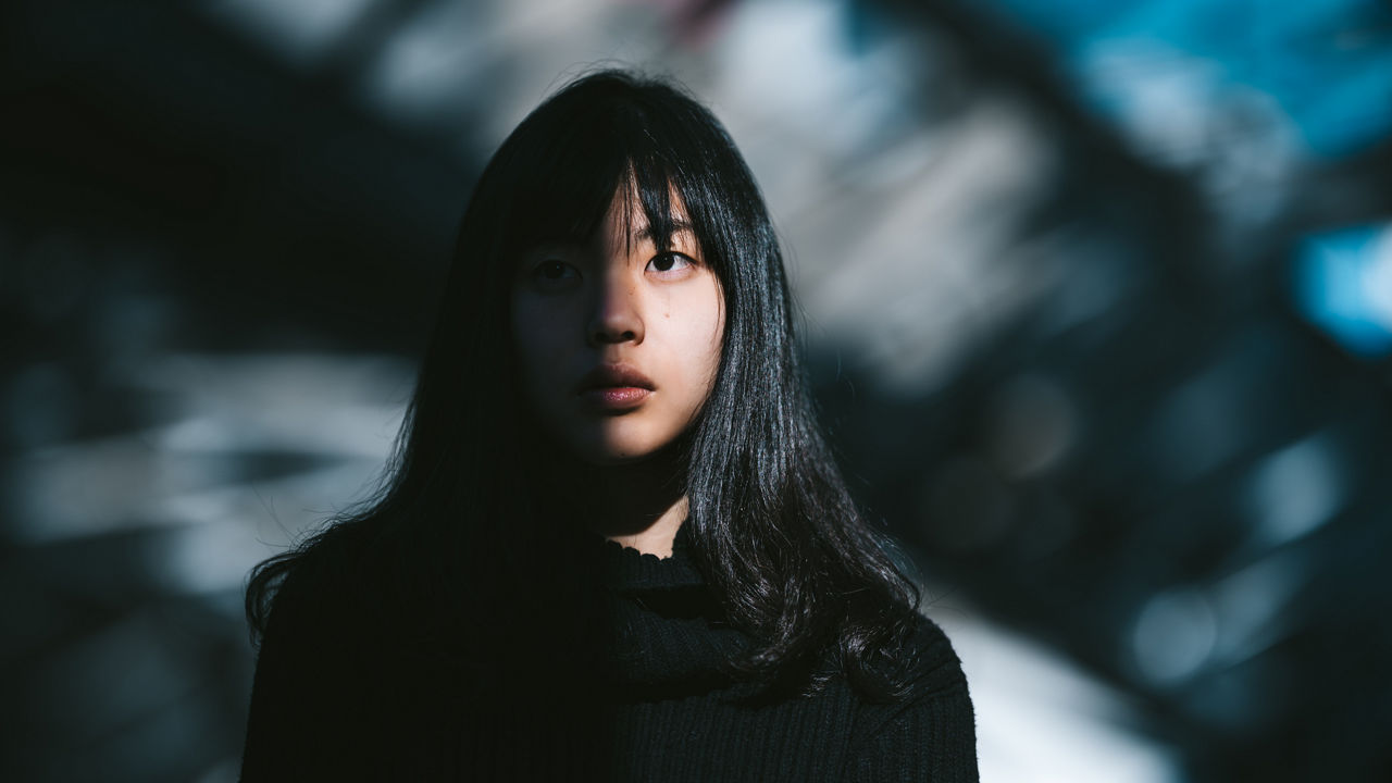 A portrait of a young Asian woman while half of her face is lit by the sun and the other half is in the shadow