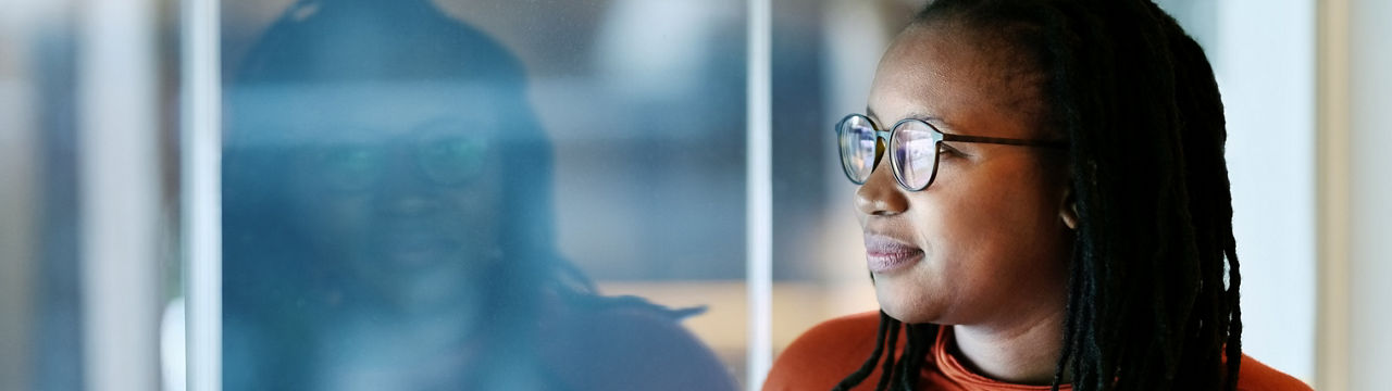 Shot of African American woman leaning to a window and looking outside thinking