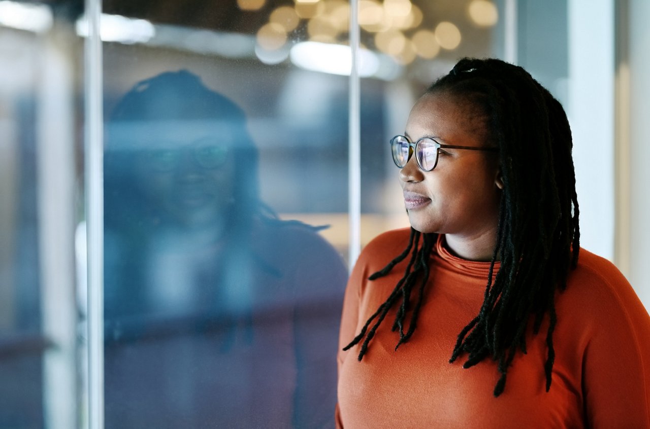 Shot of African American woman leaning to a window and looking outside thinking