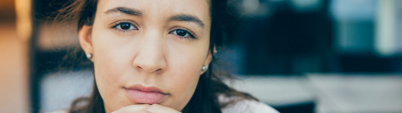 Serious face of young Latin American woman sitting at cafe. Close-up of businesswoman or female student with clasped hands looking at camera. Young woman concept