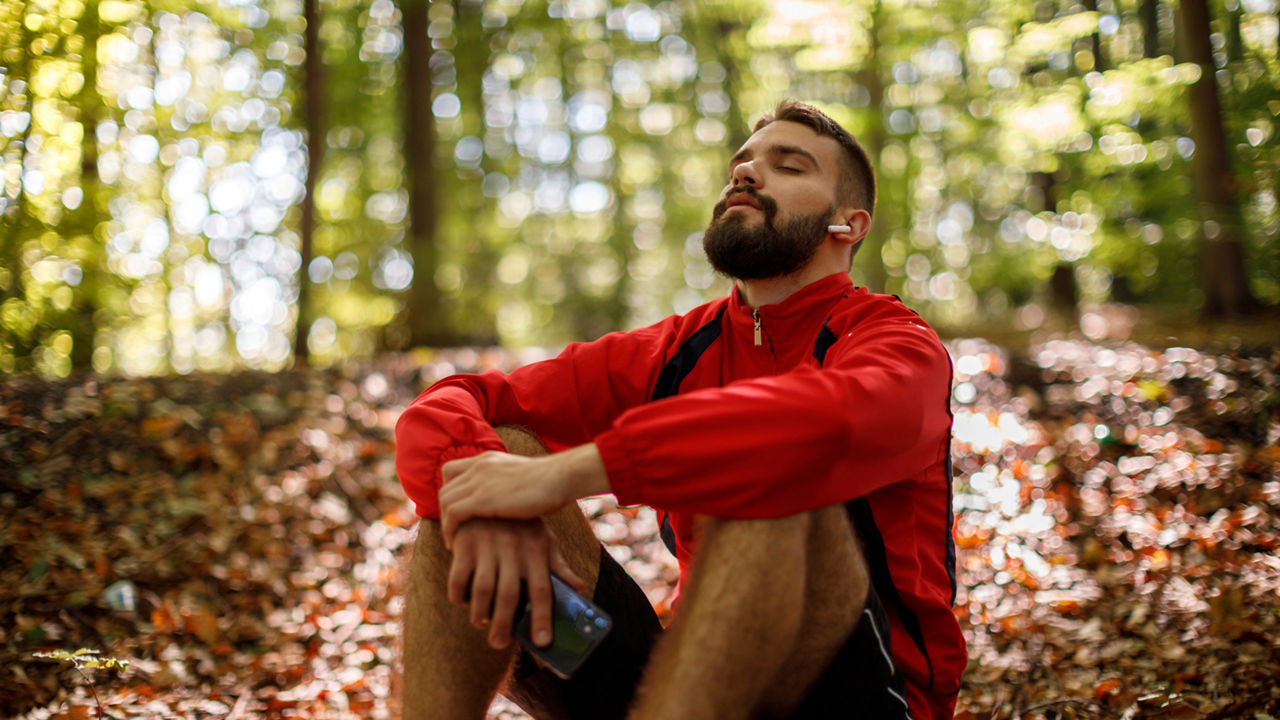 Portrait of relaxed young man with bluetooth headphones in forest