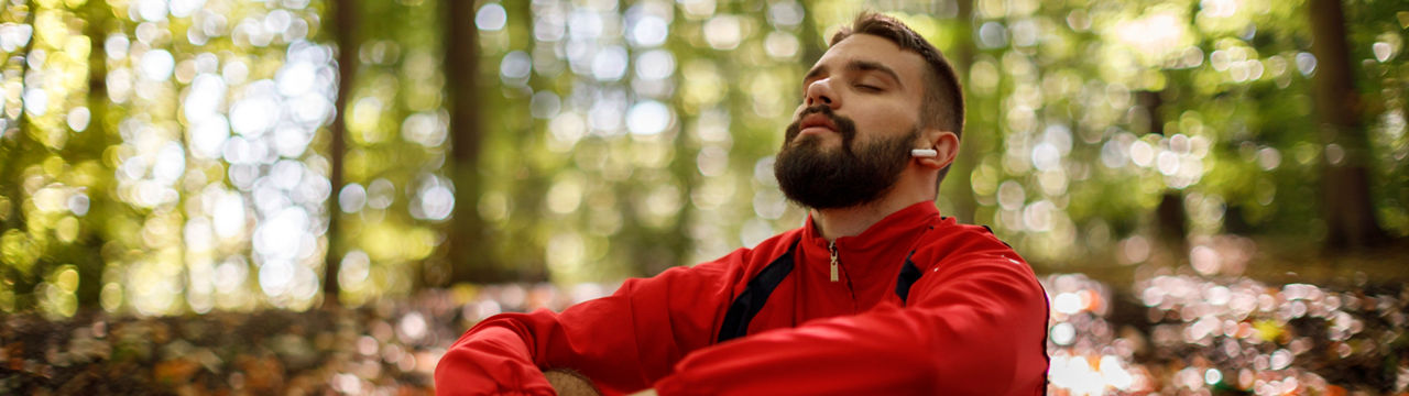 Portrait of relaxed young man with bluetooth headphones in forest