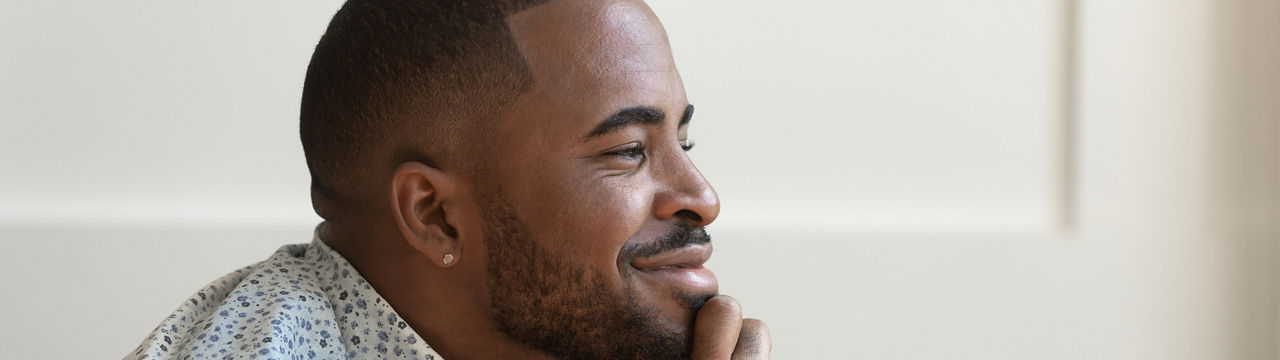 Dreamy calm African American young man looking away contemplating daydreaming sitting at home