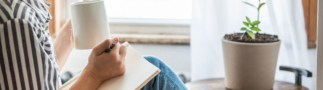 A young woman takes a break to do something analog like writing in her journal and drinking tea. This is a healthy practice for those who experience anxiety