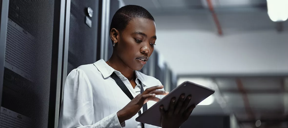 IT technician using a digital tablet in a server room. Female programmer fixing a computer system and network while doing maintenance in a datacenter. Engineer updating security software on a machine