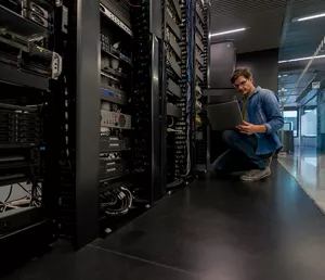 Latin American computer engineer fixing a network server at an office using his laptop - technology concepts