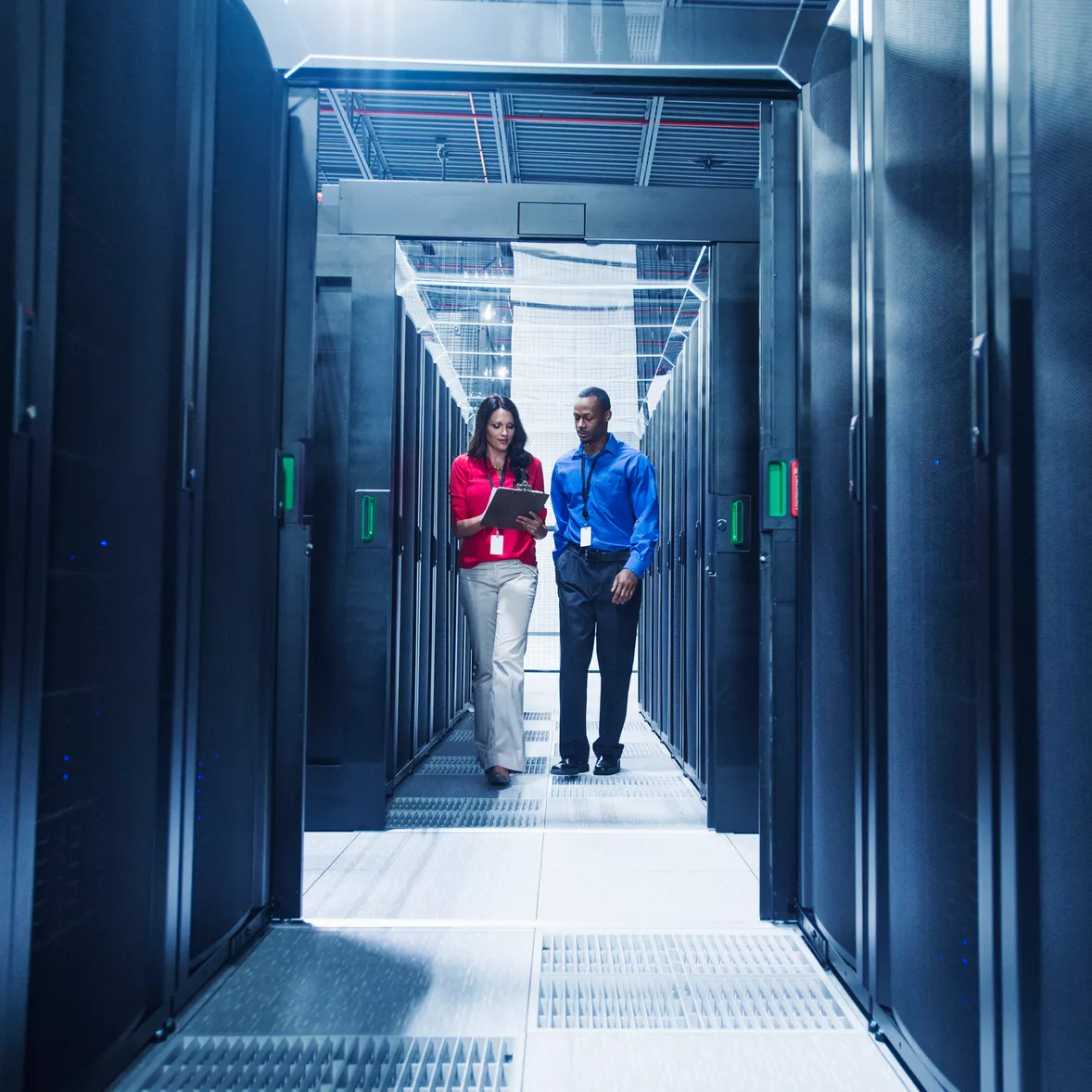 Two co-workers at a tech firm walk through a server room while discussing Green IT solutions for their company