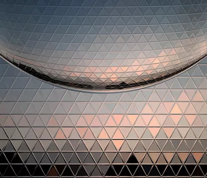 Digitally generated image of a metallic surface with triangle shape mosaic reflecting the sky and a perfect globe. The profile in the background is a generic cityscape at sunset.