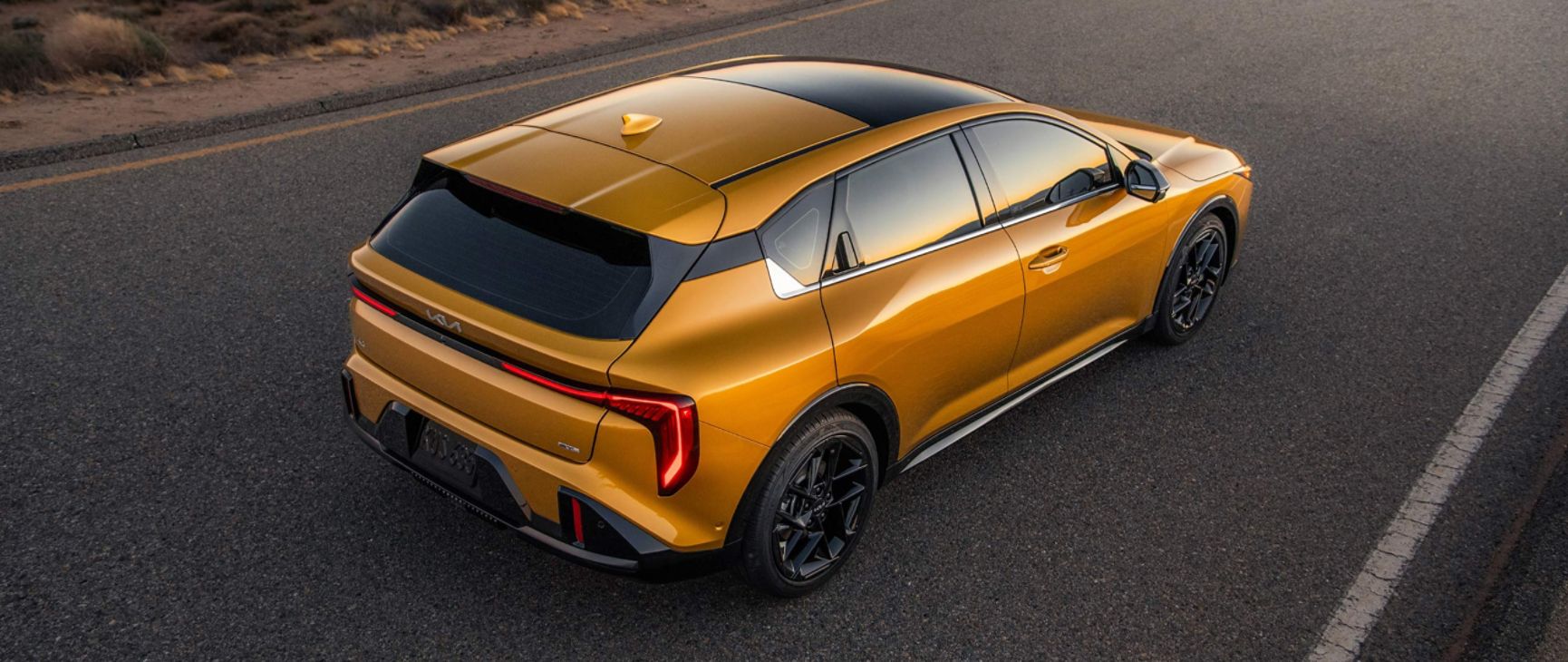 A rear top view shot of the 2026 K4 Hatchback GT-Line Turbo in a vibrant Yellow-Orange finish and sleek design while driving along a desert highway.