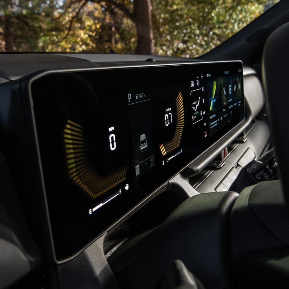 Digital cockpit of the 2027 Kia Seltos showing a wide digital display and speed and driving information, framed by a modern dashboard with trees visible through the windshield.