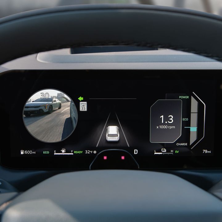 Zoomed in view of the digital instrument cluster on the Kia vehicle that features the speedometer on the left, the vehicle image in a lane in the middle, and a monitor that displays a live view of the car's blind spot on the right. 