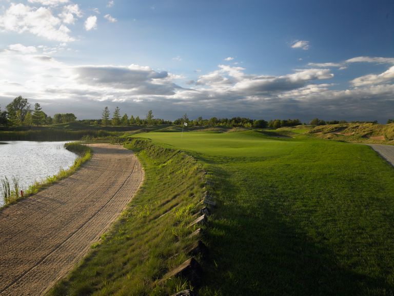 A view of the green of the third hole of the Irish Course with a pond and sand bunker on the left. 