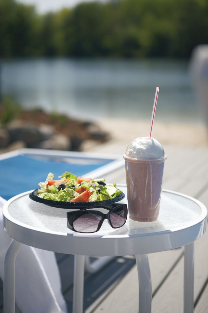 a smoothie, salad and sunglasses on a table with a lake in the background