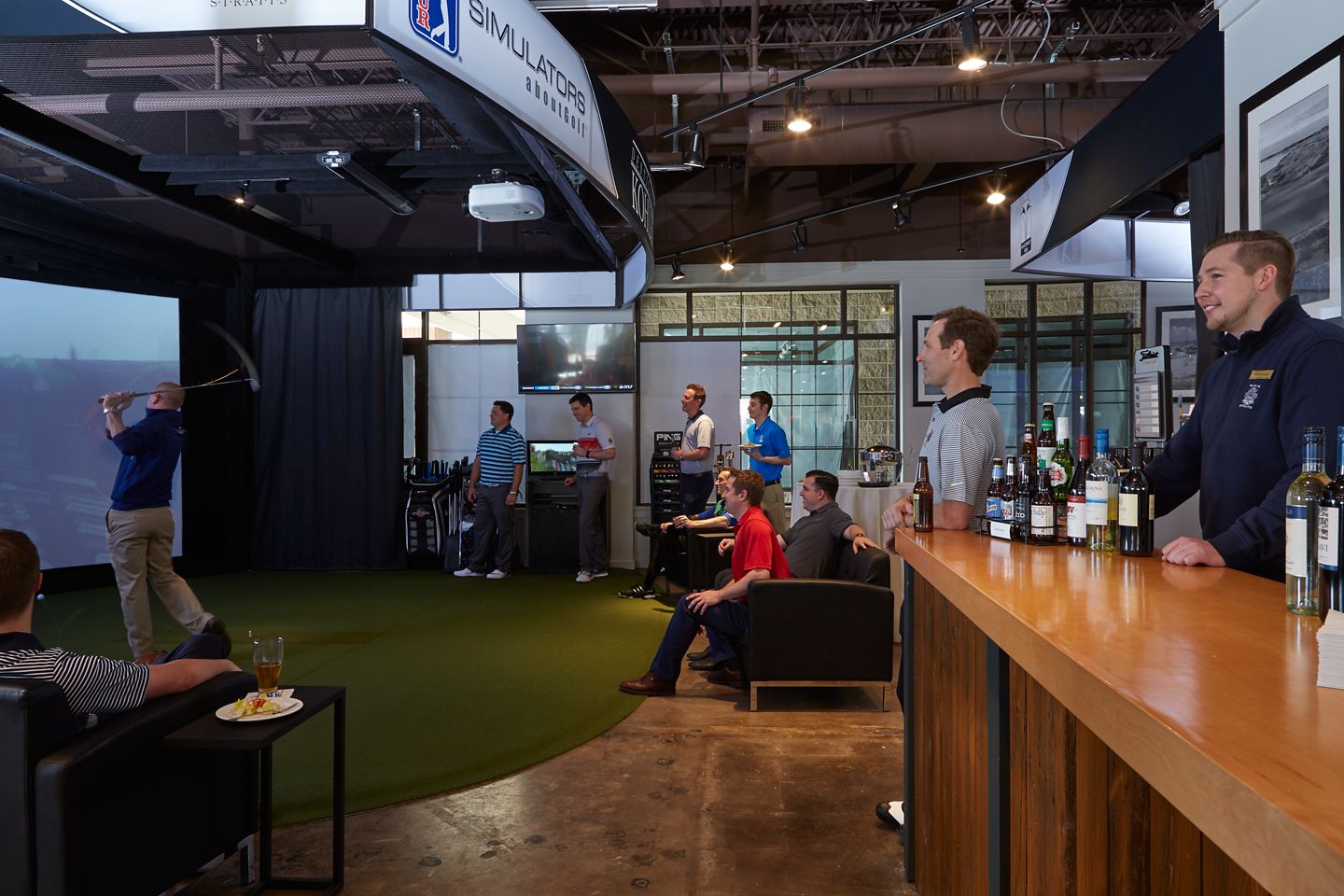 a man swinging a golf club on an indoor simulator with a group of people watching him
