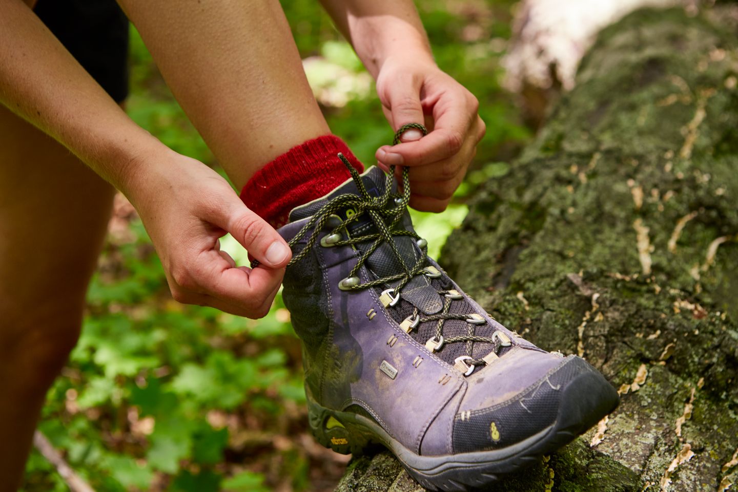 A closeup of a woman tying up her hiking boots in the forest