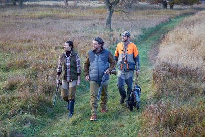 three people and a dog walking through a field with hunting equipment