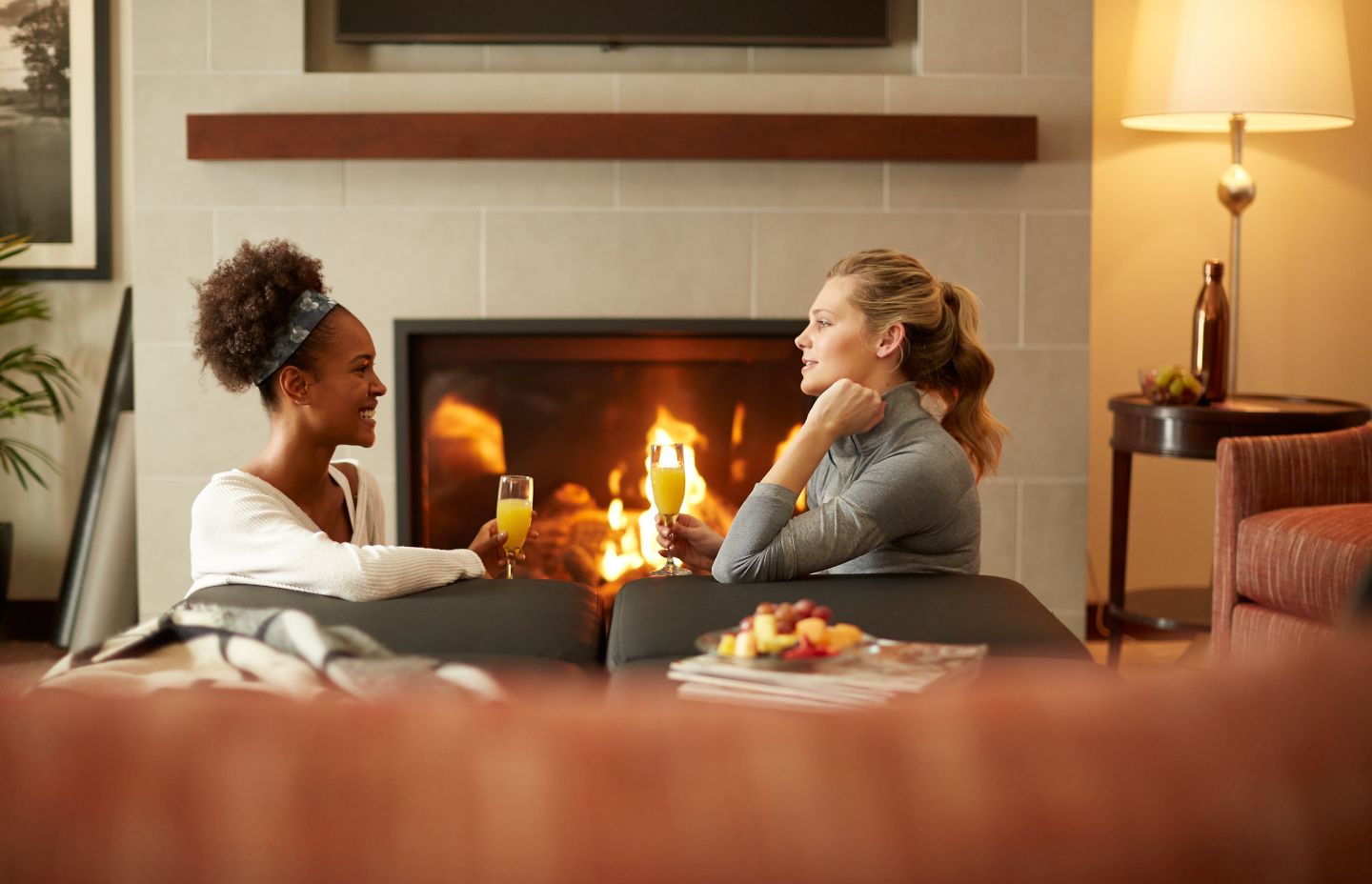 Two women sit on a couch near a fireplace in their room at the Inn on Woodlake