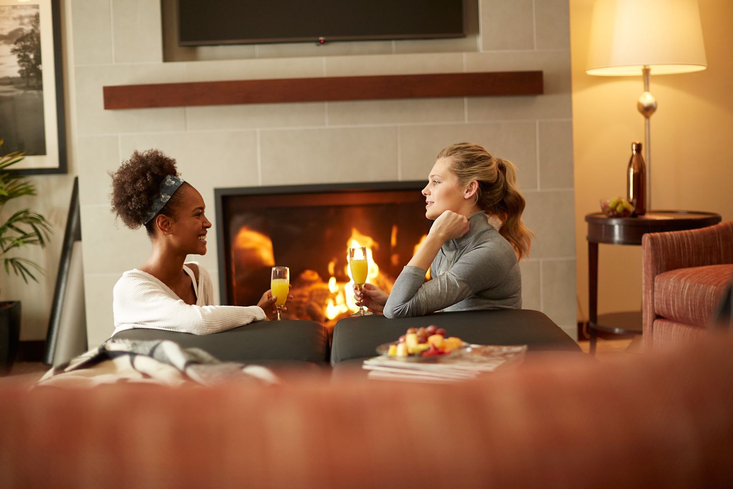 Two women sit on a couch near a fireplace in their room at the Inn on Woodlake