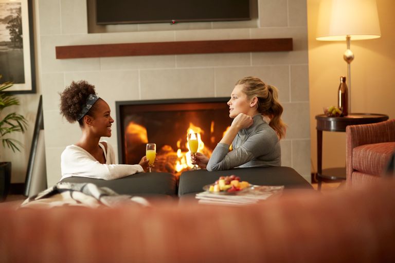 Two women enjoying mimosas in front a of a fireplace
