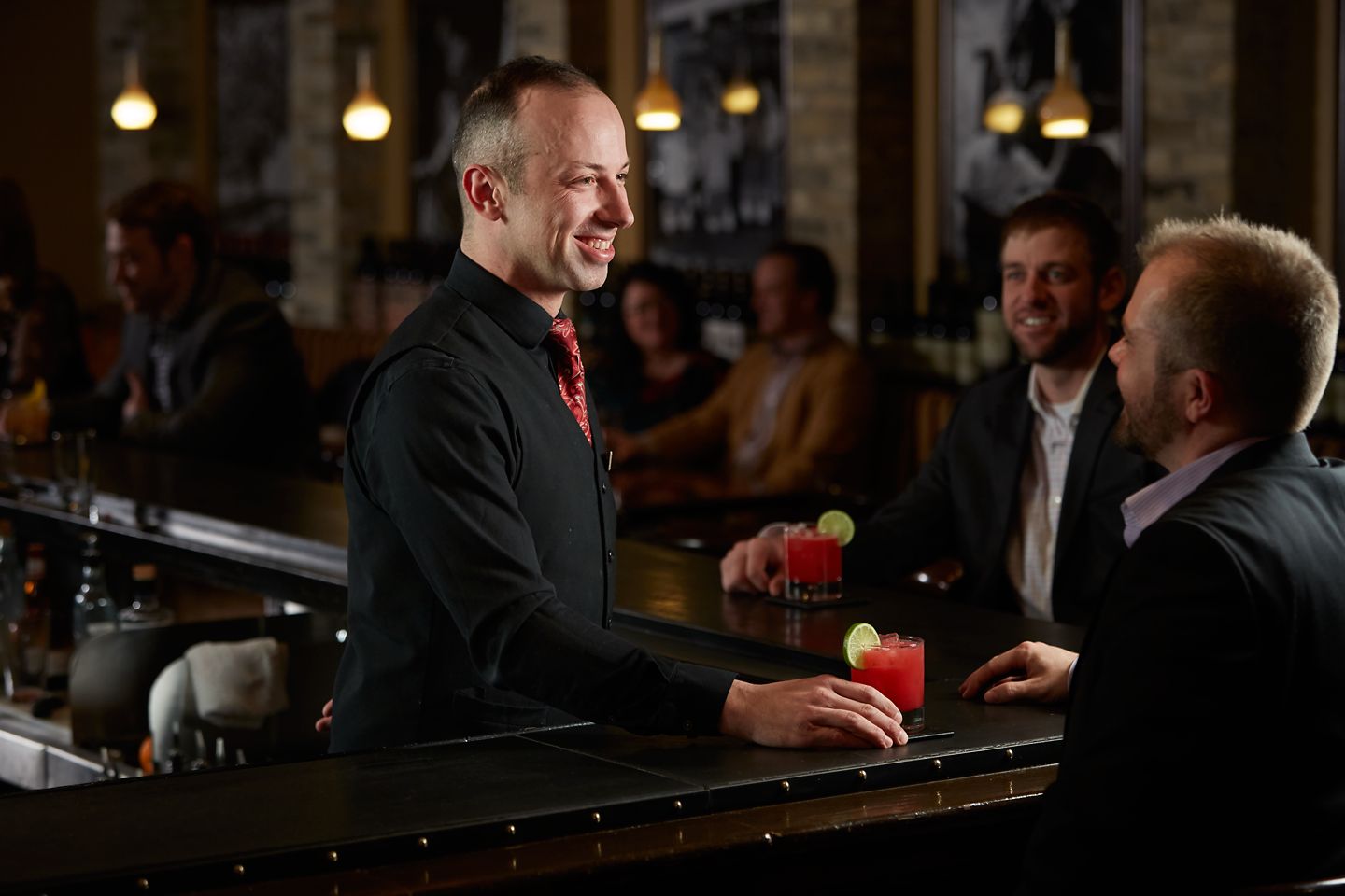 a mixologist behind a bar smiling at a guest