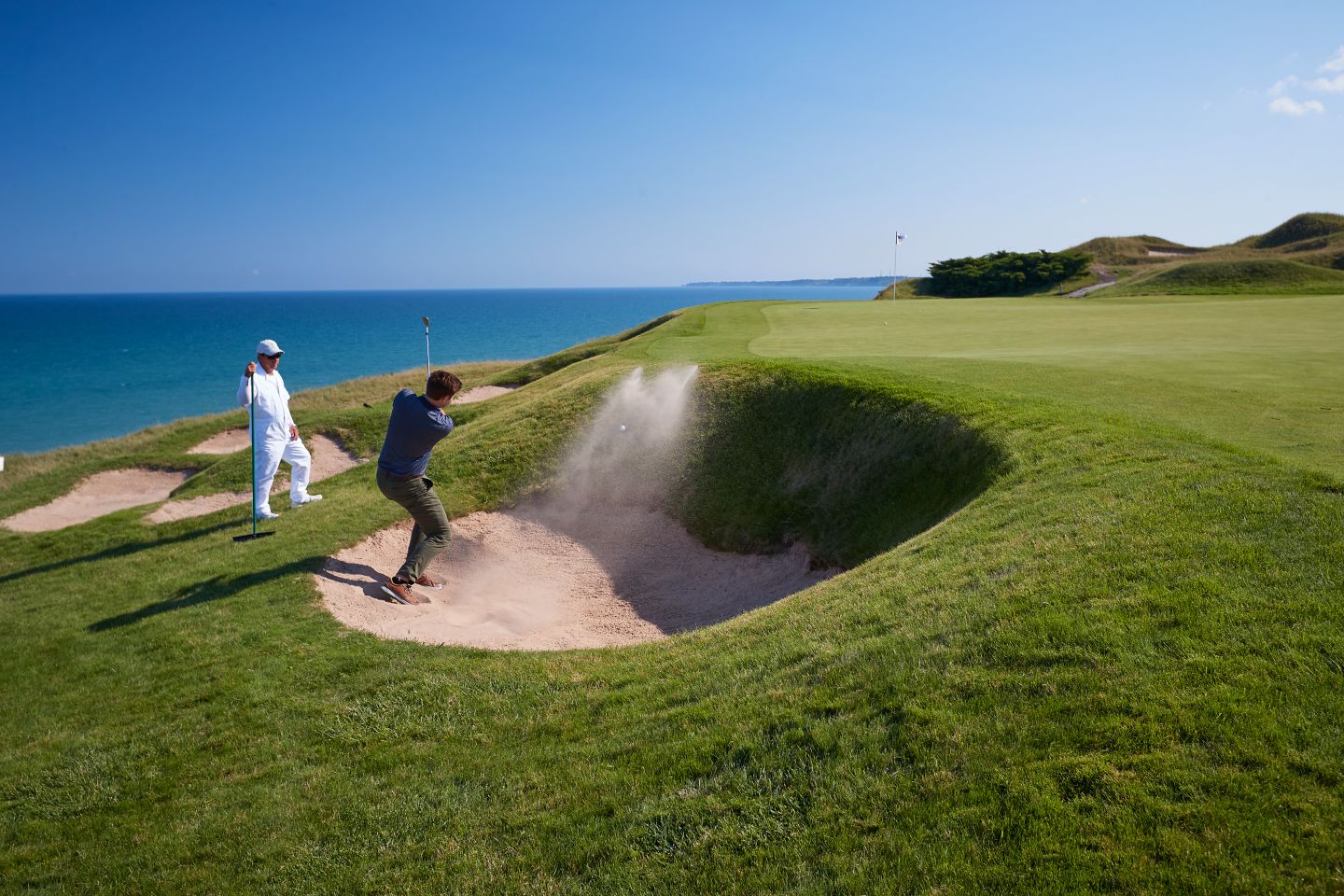 a golfer hitting out of a greenside bunker with sand splashing
