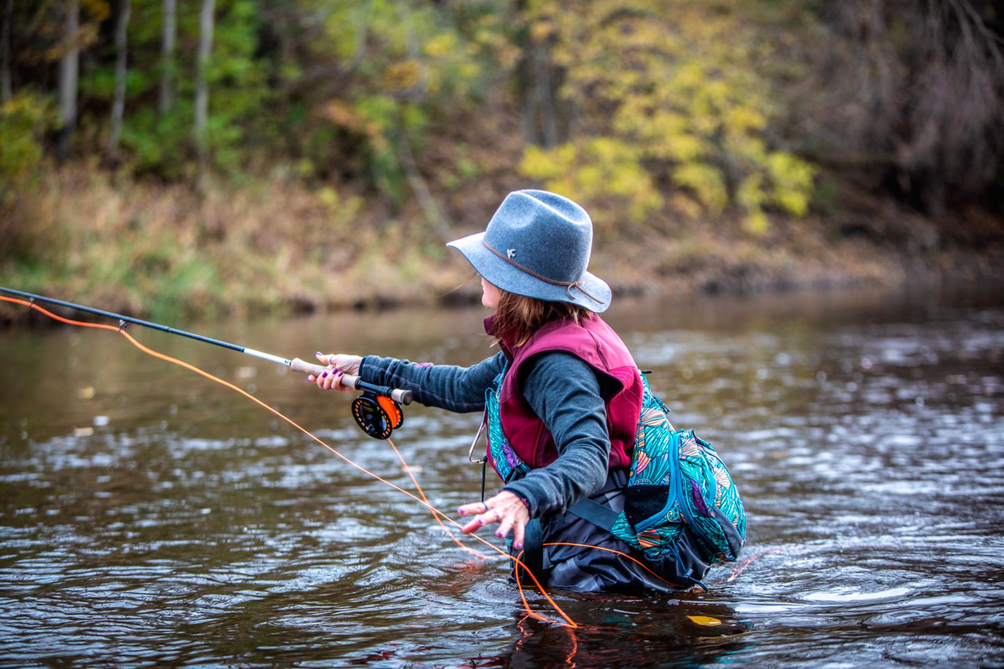 A woman in a hat fly fishing in the Sheboygan River in summertime
