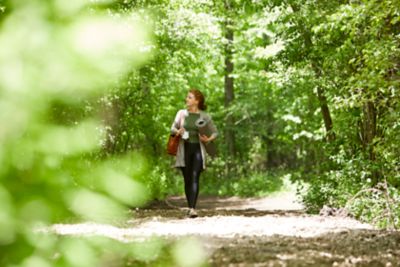 A woman walking through the woods with a yoga mat