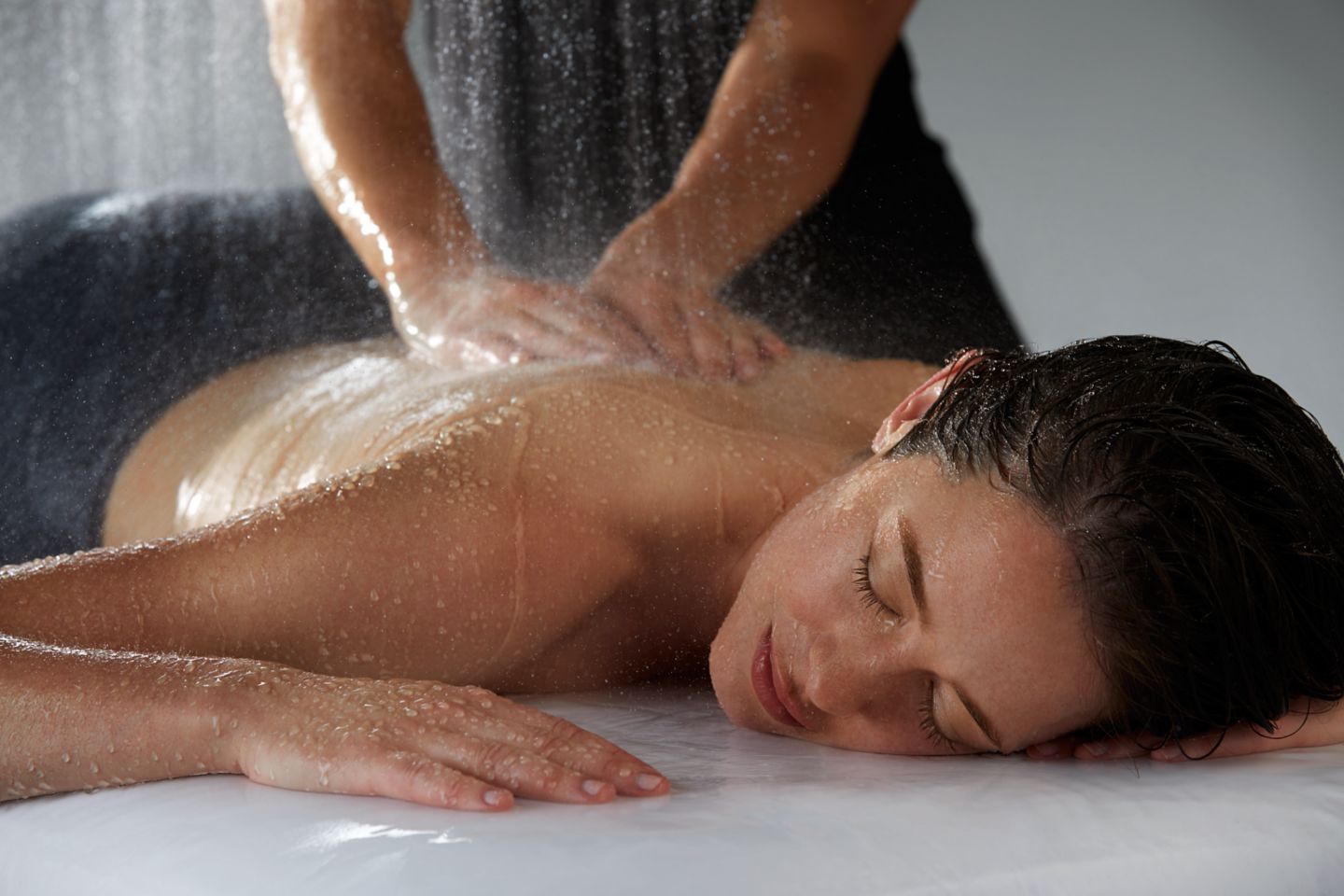 a woman laying on her stomach getting a massage while water is spraying down on her