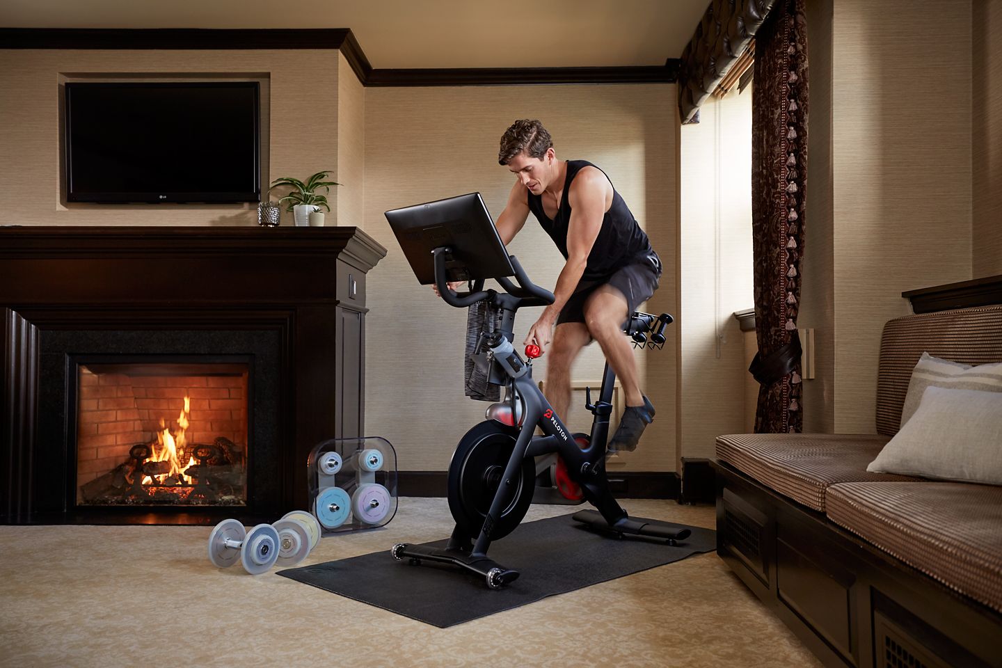 A man uses a Peloton bike near the fireplace in his room at The American Club