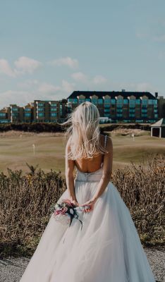 Bride standing on West Sands Beach looking towards the Old Course Hotel, Golf Resort & Spa