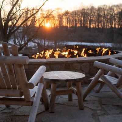 two chairs next to an outdoor fire with the sun setting in the distance