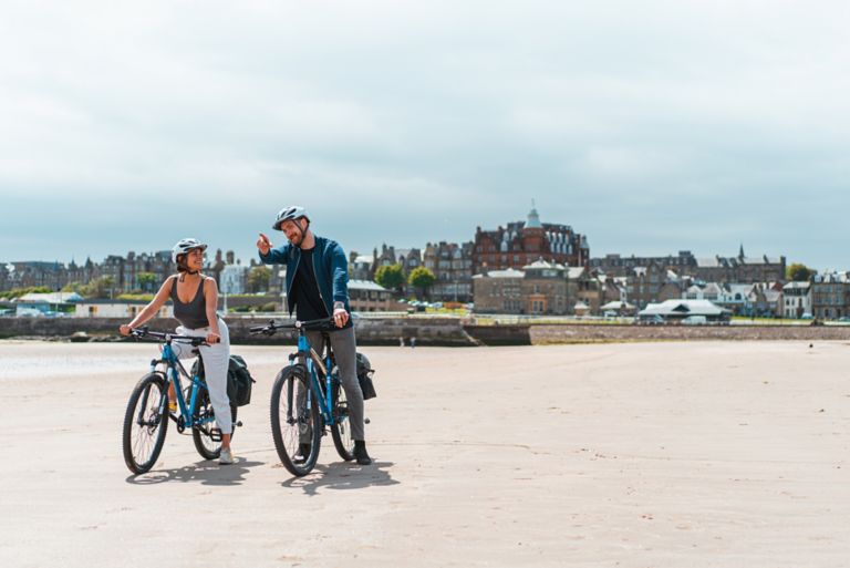 Man and woman cycling on West Sands Beach in St Andrews