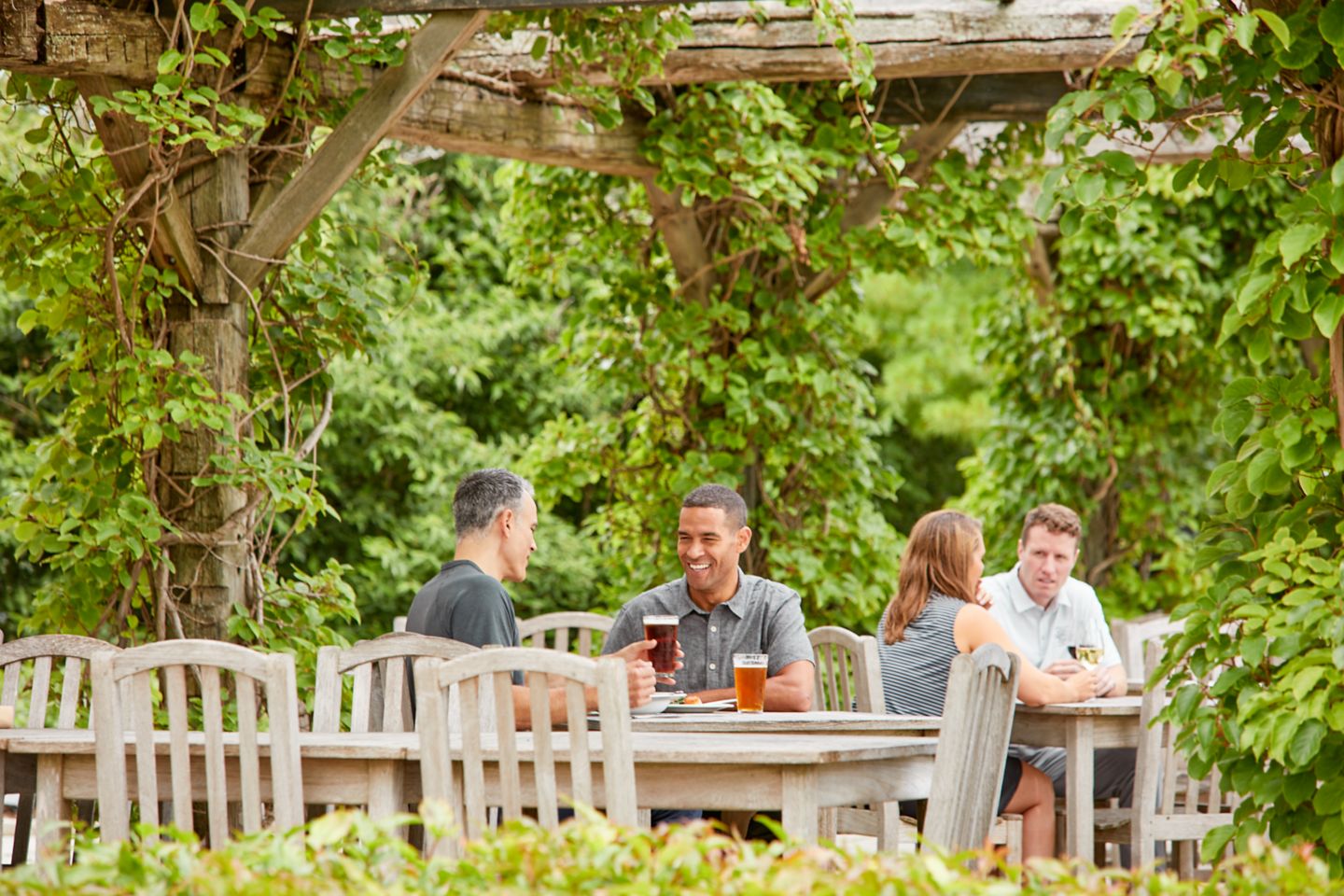 two gentlemen sitting outside at a dining table laughing and enjoying glasses of beer