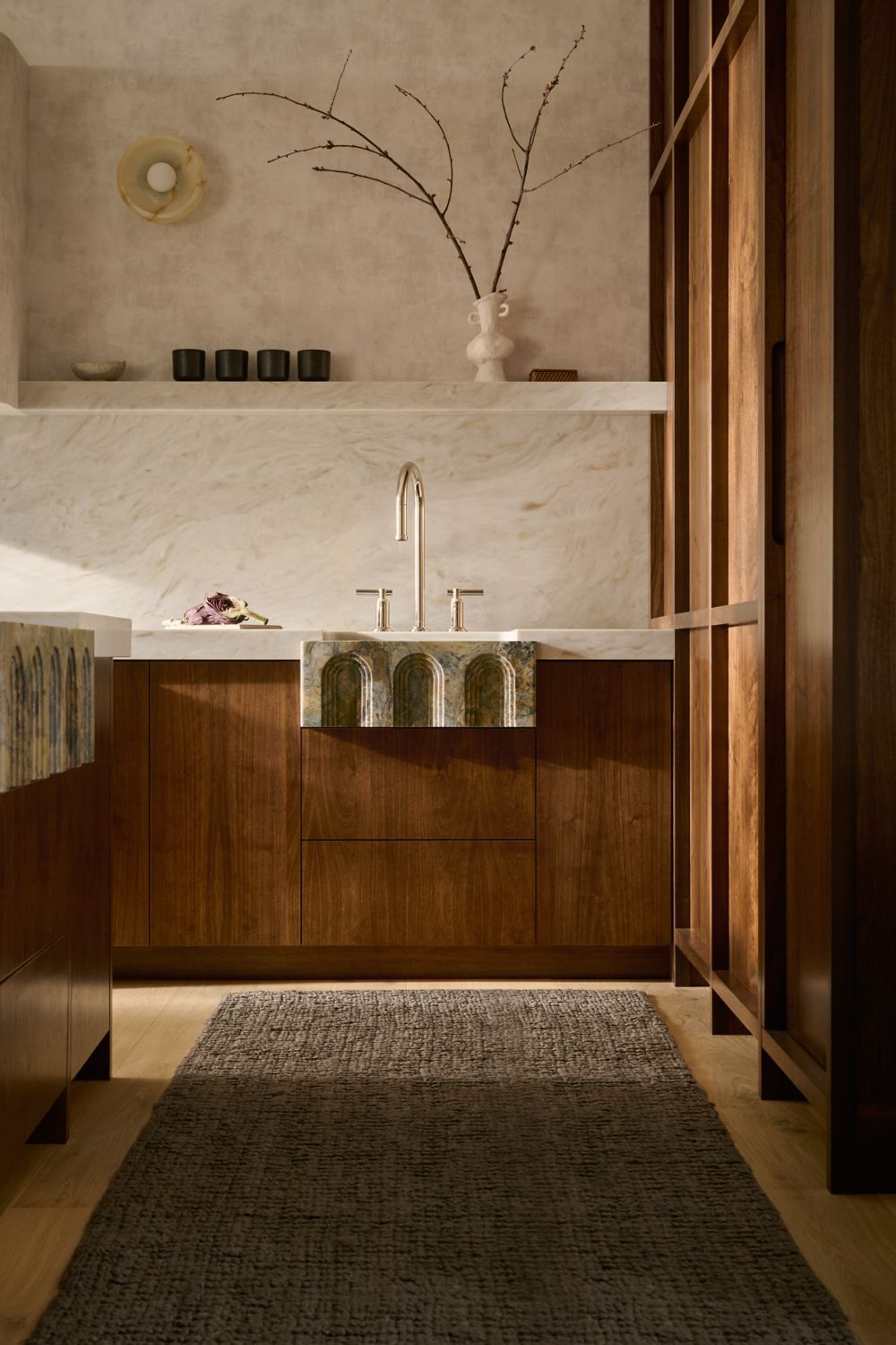 Dark wood bathroom vanity with marble countertop, decorative branches, and warm lighting.