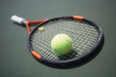 A closeup of a tennis ball sitting on a tennis racket on a tennis court