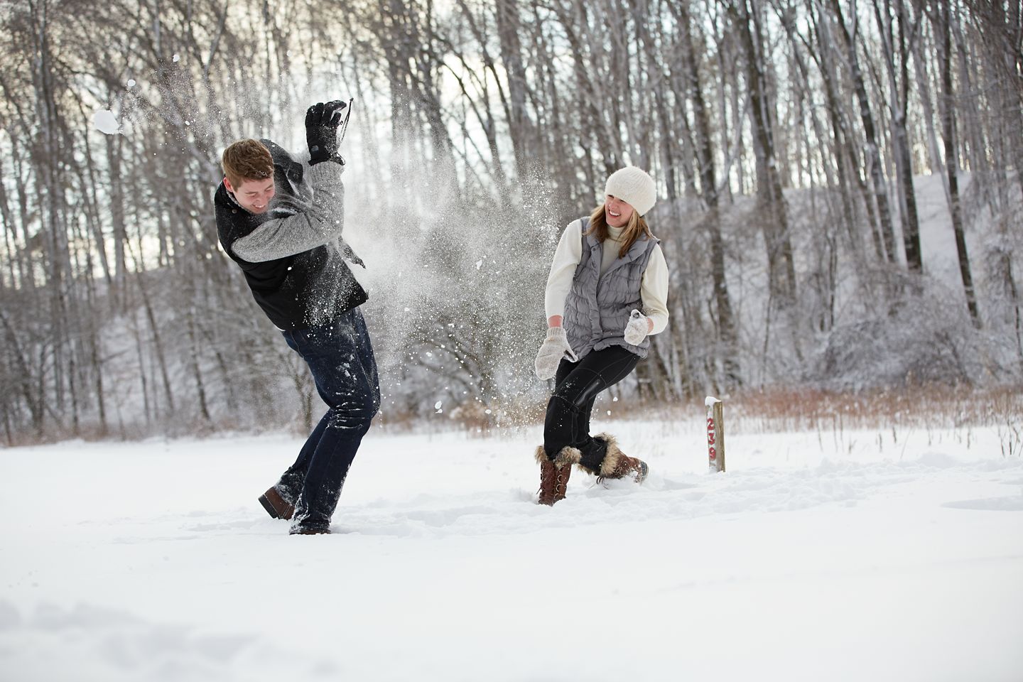 A man and a woman have a snowball fight in a snowy field in the winter