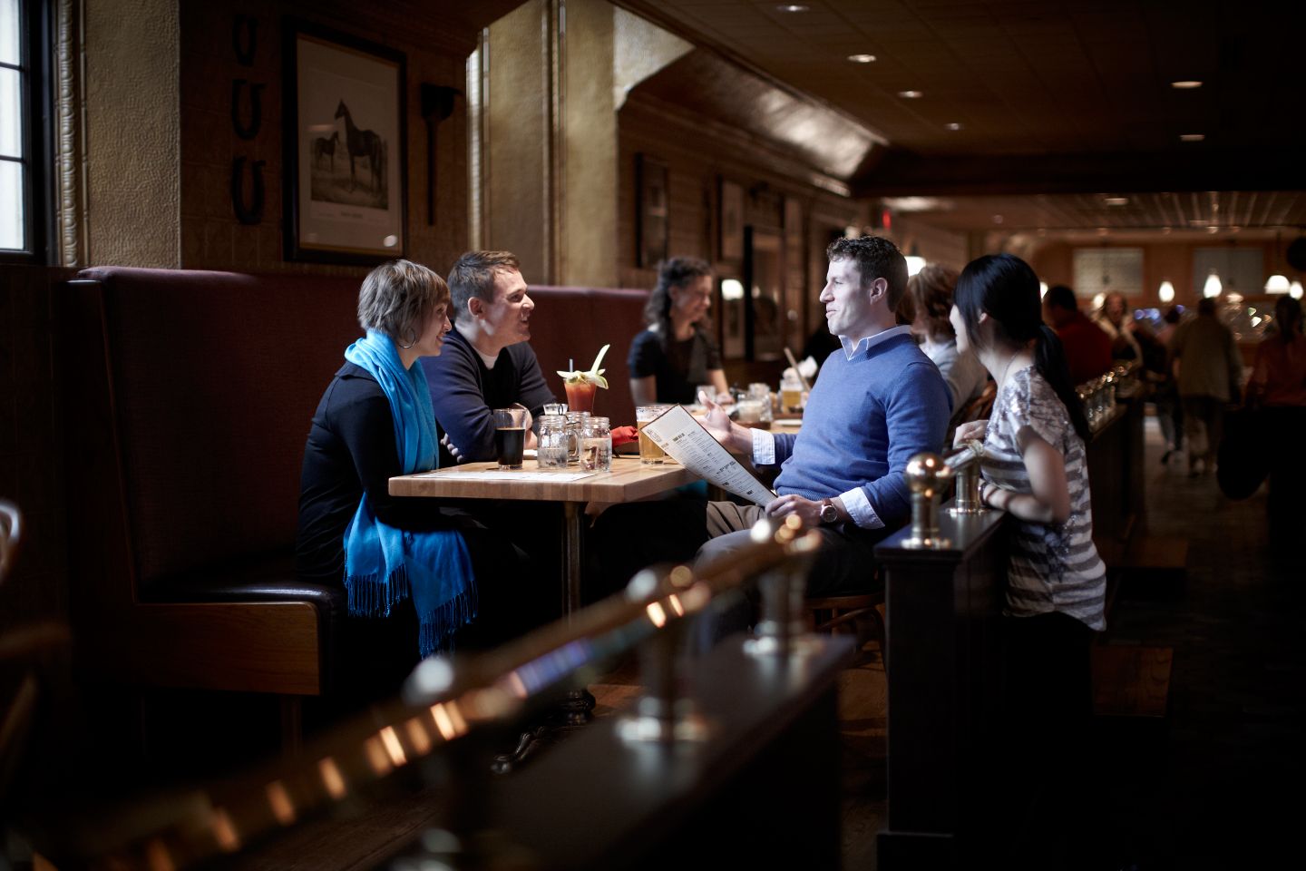 three people sitting at a restaurant table with one person standing, all of them talking
