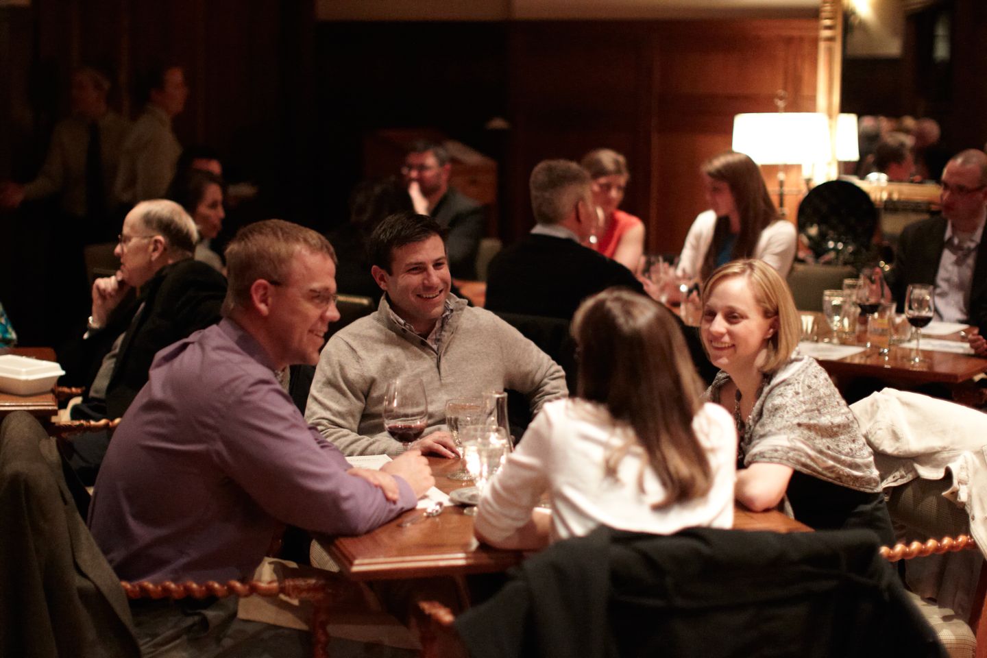 a table of people in a full dining room laughing and having drinks