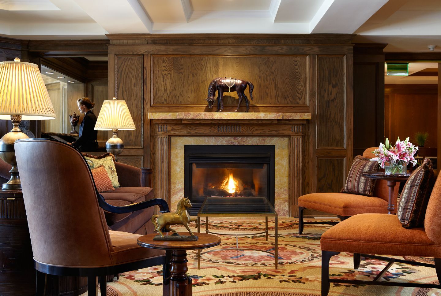 A woman checks into the hotel near the fireplace surrounded by orange chairs