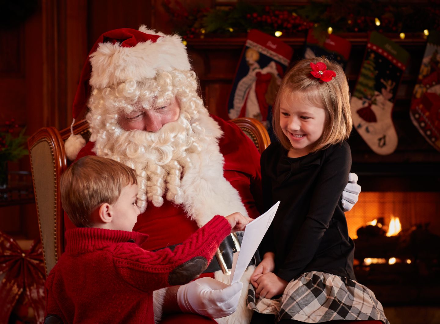 two kids sitting on santa's lap in front of a lit fireplace