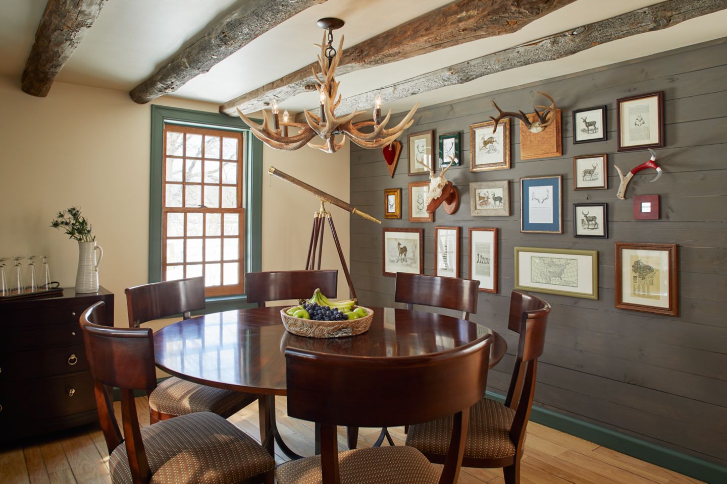 The round dining table and 6 chairs with antler lighting fixture along with various deer paintings on the walls