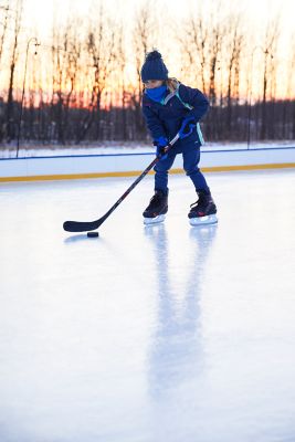a child skating with a hockey stick on an outdoor rink with the sun setting in the background